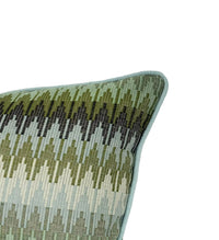 A close-up of a woven throw pillow corner showing a geometric pattern in shades of olive green, and light blue, finished with a light blue piped edge.