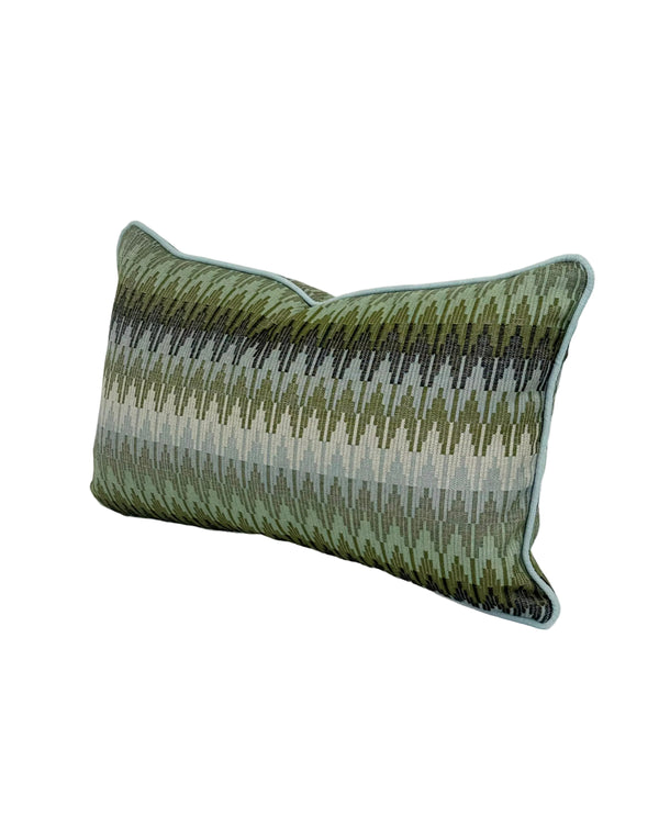 A rectangular lumbar throw pillow with a textured, woven chevron pattern in shades of olive green, and blues, finished with a light blue piped edge, shown on a white background. Finished in a light blue trim.