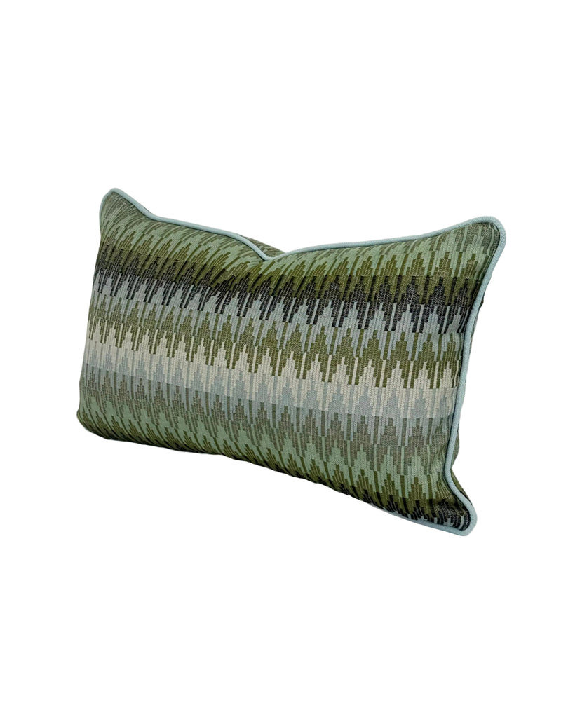 A rectangular lumbar throw pillow with a textured, woven chevron pattern in shades of olive green, and blues, finished with a light blue piped edge, shown on a white background. Finished in a light blue trim.