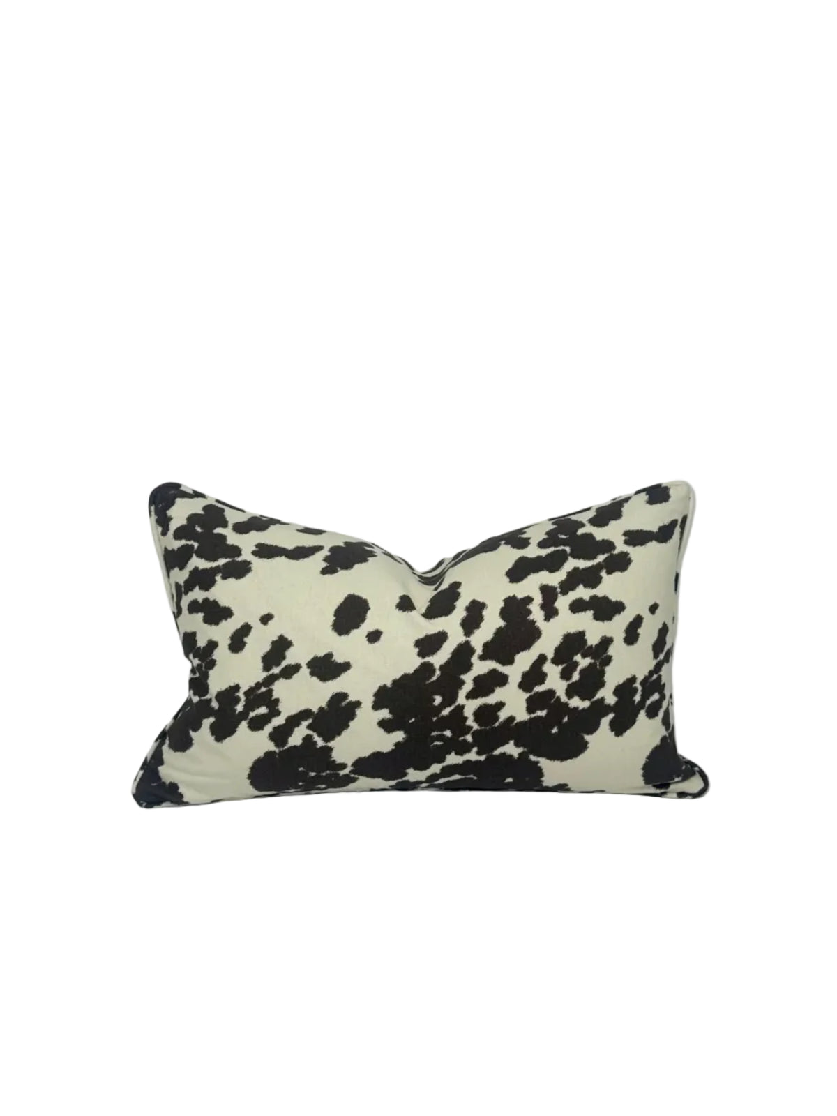 A rectangular lumbar throw pillow featuring a dark brown cow print pattern on a cream background, photographed against a white studio backdrop.