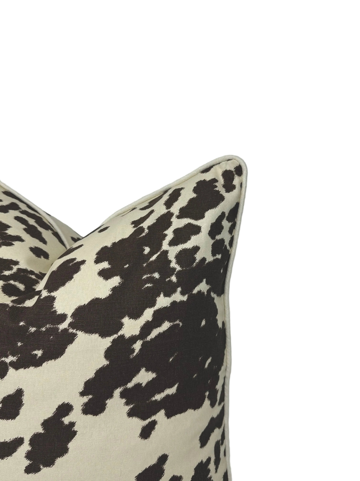 A close-up of a decorative throw pillow with a brown cow-print pattern on a cream background, shown against a plain white screen backdrop.