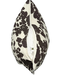 A square decorative throw pillow with a cow print pattern in dark brown and Cream, shown with its zipper opening on bottom to reveal the white pillow insert.