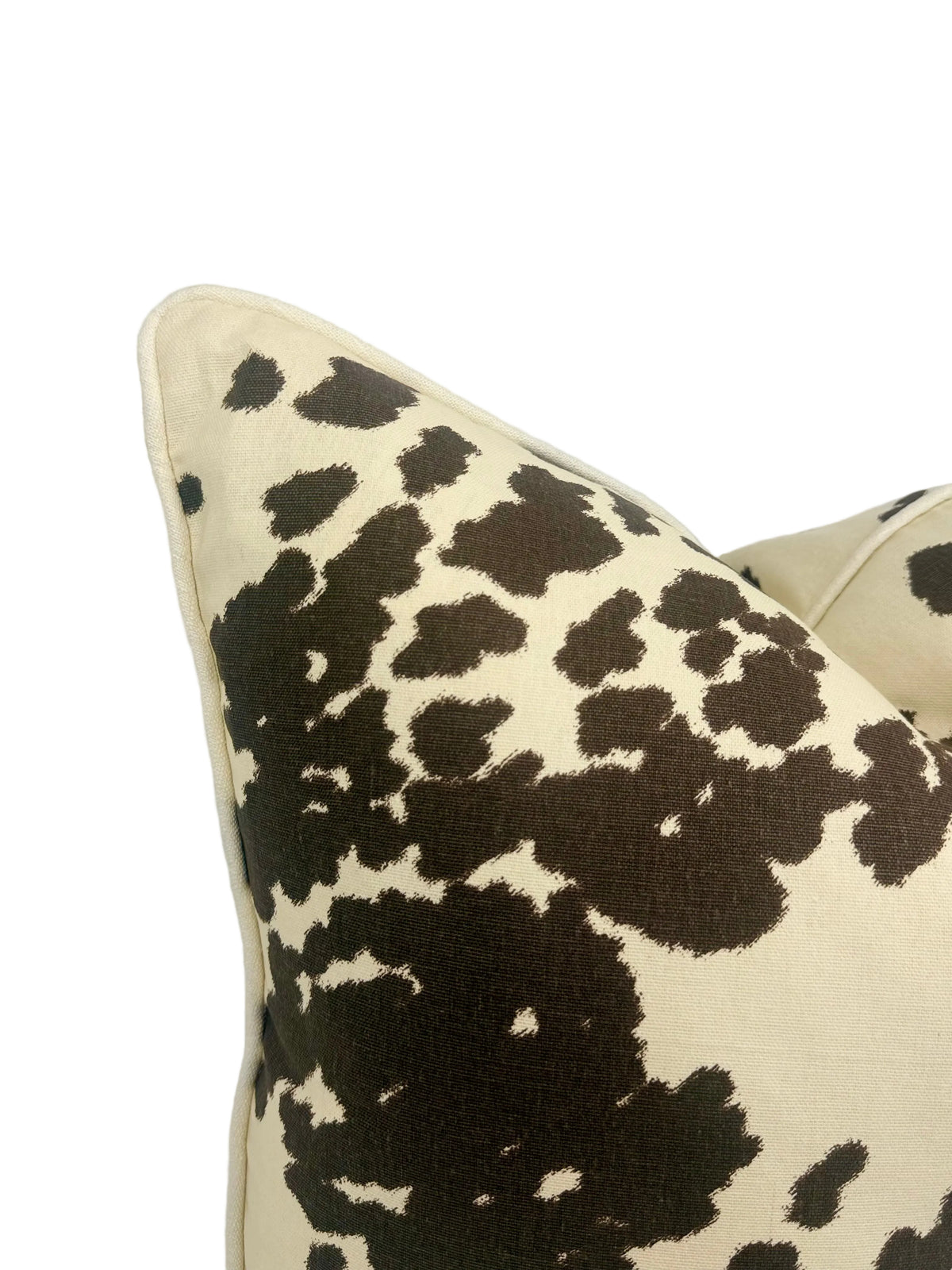 Close-up of a decorative throw pillow featuring a dark brown cow-print pattern on a cream-colored fabric, set against a plain white background.